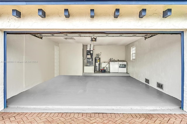 garage featuring heating unit, electric water heater, and washer and clothes dryer