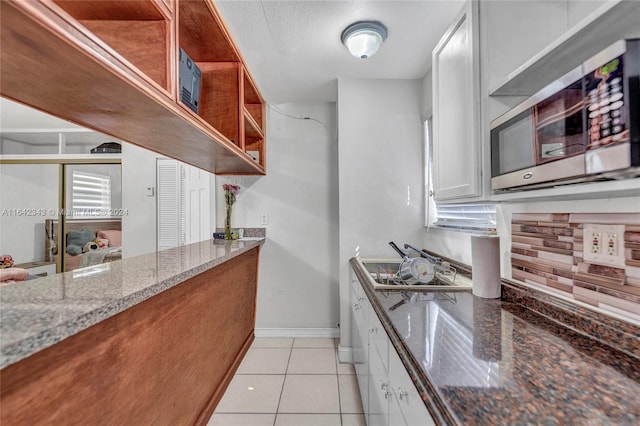 kitchen with white cabinetry, a textured ceiling, stone countertops, and light tile patterned flooring