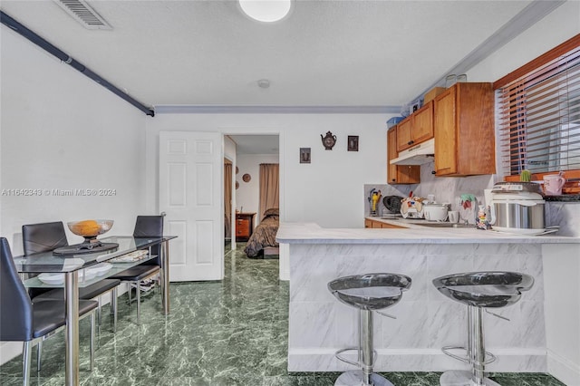 kitchen featuring tasteful backsplash, kitchen peninsula, a textured ceiling, a kitchen bar, and ornamental molding