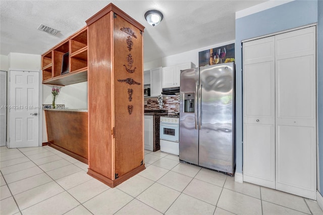 kitchen with a textured ceiling, tasteful backsplash, white range oven, light tile patterned floors, and stainless steel fridge