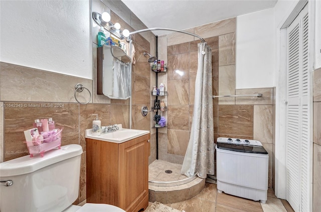 bathroom with tile walls, washer / clothes dryer, walk in shower, vanity, and toilet