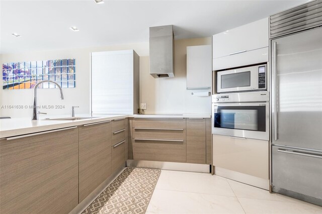 kitchen featuring light tile patterned flooring, built in appliances, sink, and wall chimney exhaust hood