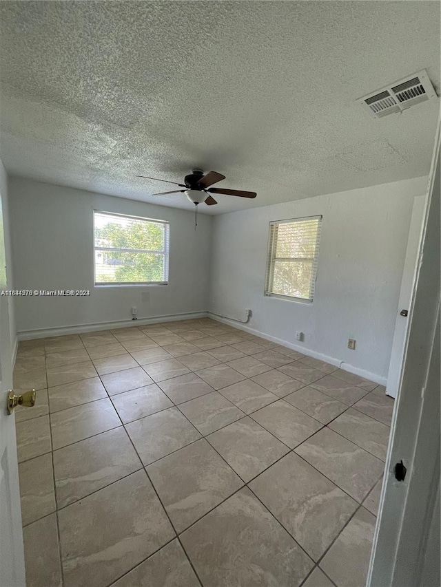 empty room with ceiling fan, light tile patterned floors, and a textured ceiling