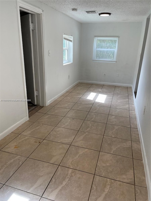 empty room with a textured ceiling and light tile patterned flooring