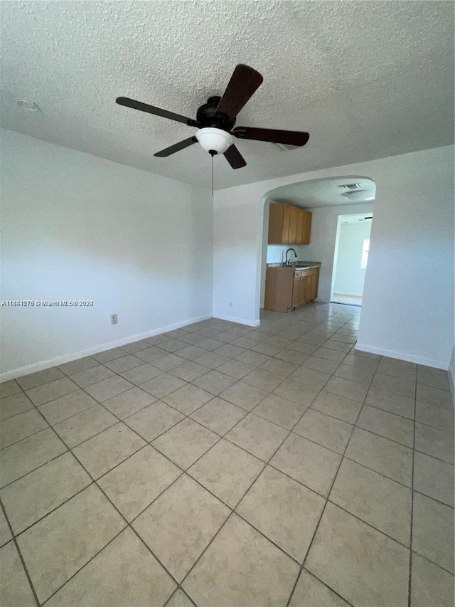 unfurnished living room with ceiling fan, light tile patterned floors, sink, and a textured ceiling