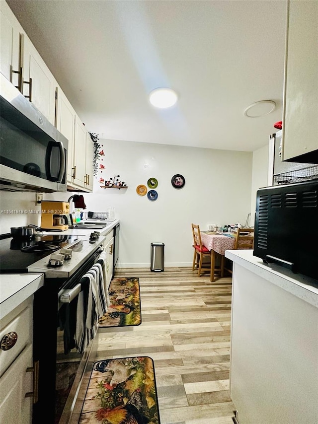 kitchen featuring sink, electric range oven, light hardwood / wood-style floors, and white cabinetry