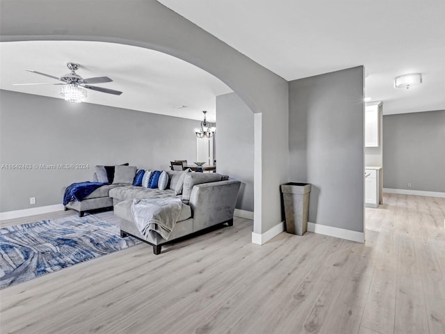 living room featuring ceiling fan with notable chandelier and light wood-type flooring