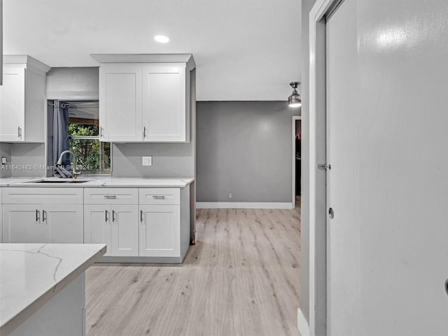 kitchen with light hardwood / wood-style floors, sink, light stone counters, and white cabinetry