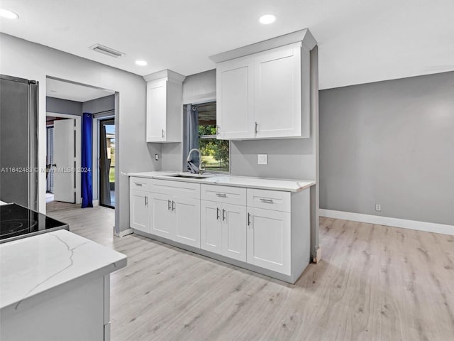 kitchen featuring sink, light hardwood / wood-style flooring, light stone counters, stainless steel refrigerator, and white cabinetry