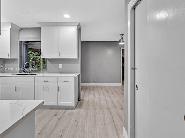 kitchen featuring sink, white cabinets, light stone counters, and light wood-type flooring