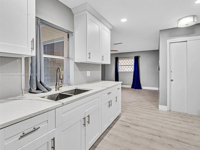 kitchen featuring sink, light wood-type flooring, white cabinets, and light stone countertops