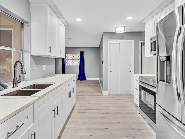 kitchen with sink, light stone counters, light hardwood / wood-style floors, stainless steel appliances, and white cabinets