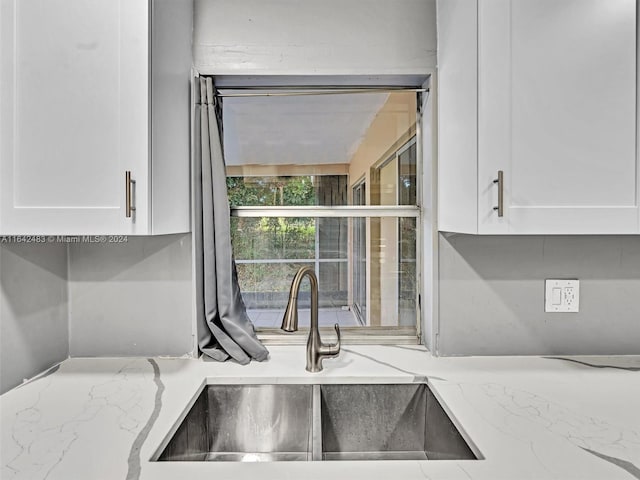 kitchen featuring sink, light stone counters, and white cabinetry