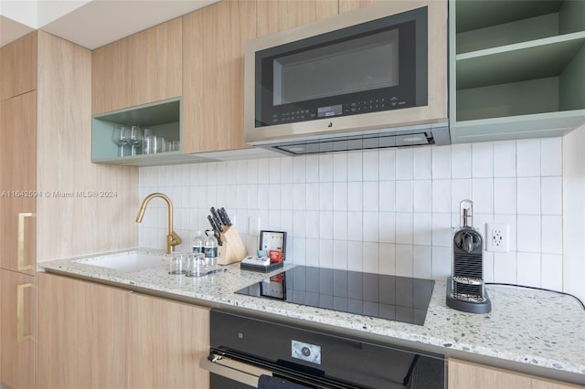 kitchen with backsplash, sink, light stone countertops, and black appliances