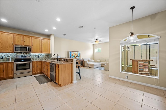 kitchen featuring a kitchen bar, appliances with stainless steel finishes, kitchen peninsula, pendant lighting, and light stone countertops