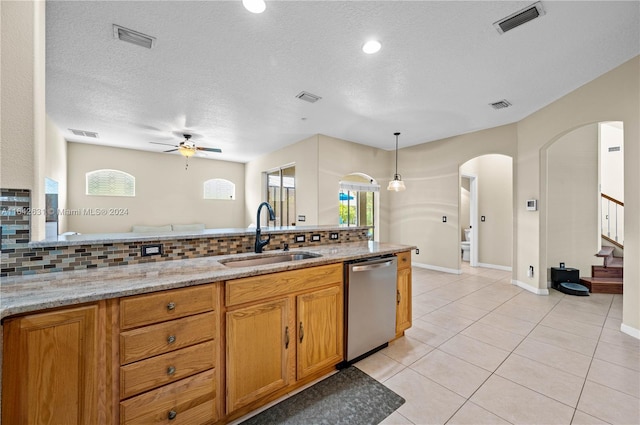 kitchen with sink, backsplash, hanging light fixtures, stainless steel dishwasher, and light stone counters