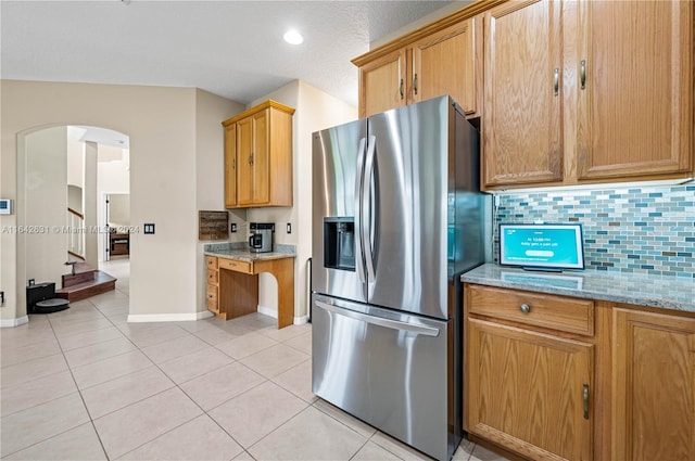 kitchen featuring light stone countertops, stainless steel fridge with ice dispenser, decorative backsplash, and light tile patterned floors