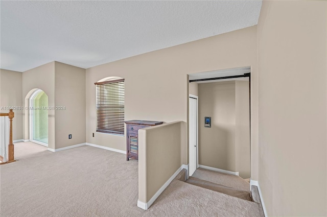 corridor with light colored carpet and a textured ceiling