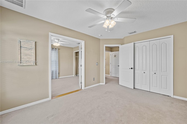 unfurnished bedroom featuring ceiling fan, light colored carpet, a textured ceiling, and a closet