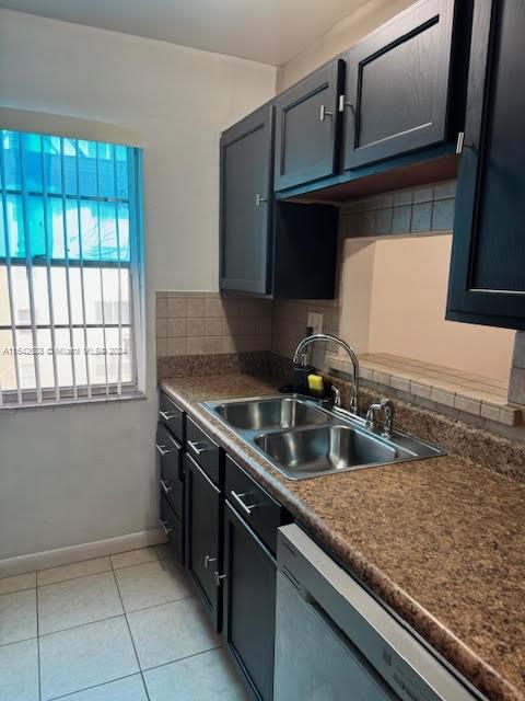 kitchen featuring backsplash, light tile patterned floors, stainless steel dishwasher, and sink