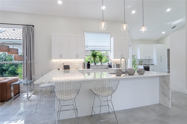 kitchen with decorative backsplash, a breakfast bar, white cabinetry, light tile patterned floors, and decorative light fixtures