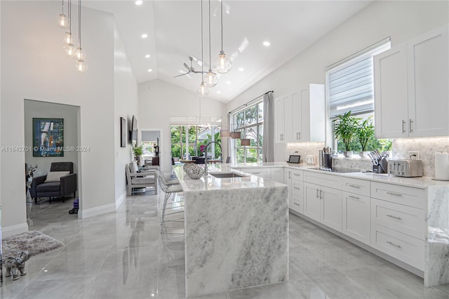 kitchen featuring sink, light stone countertops, an island with sink, pendant lighting, and white cabinets