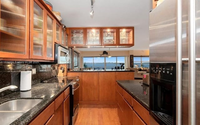 kitchen with sink, light hardwood / wood-style flooring, stainless steel appliances, and dark stone counters