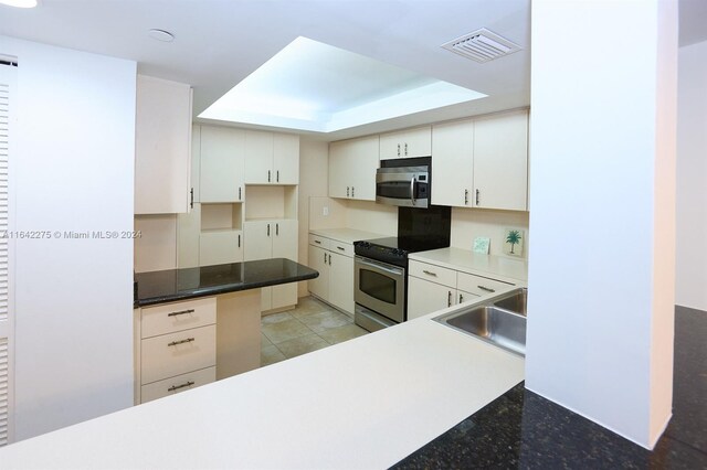 kitchen with white cabinets, light tile patterned floors, stainless steel appliances, sink, and a raised ceiling