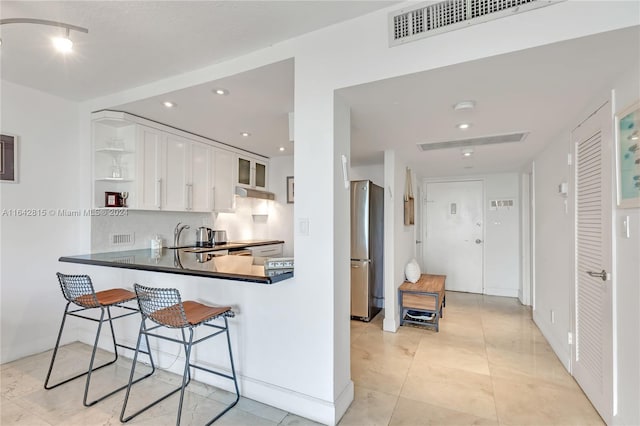 kitchen featuring kitchen peninsula, stainless steel fridge, backsplash, a breakfast bar, and white cabinets