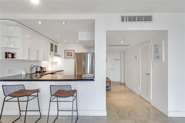 kitchen featuring a kitchen breakfast bar, tasteful backsplash, kitchen peninsula, stainless steel fridge, and white cabinets