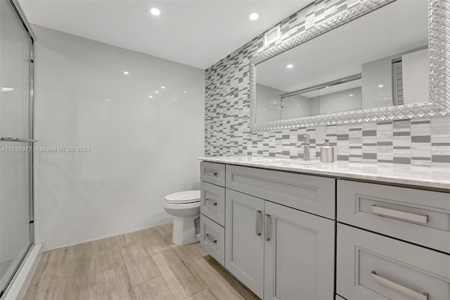 bathroom featuring toilet, an enclosed shower, hardwood / wood-style floors, vanity, and backsplash