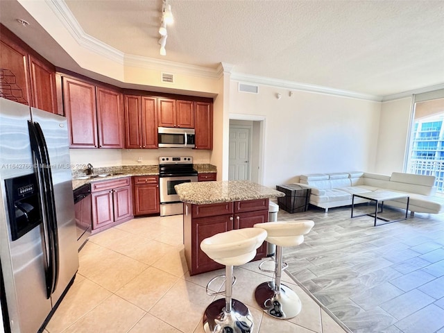 kitchen with light stone countertops, ornamental molding, a textured ceiling, appliances with stainless steel finishes, and a kitchen island