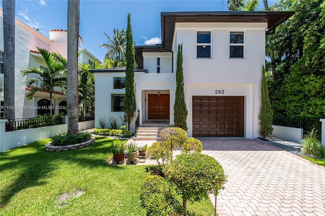 modern home with an attached garage, fence, decorative driveway, stucco siding, and a front yard