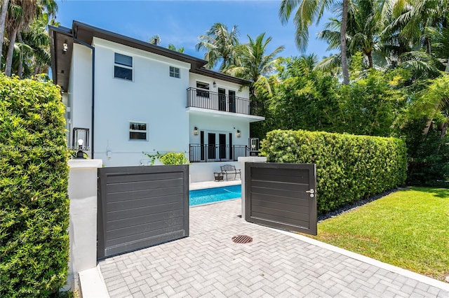 back of property with a patio, stucco siding, a balcony, and an outdoor pool