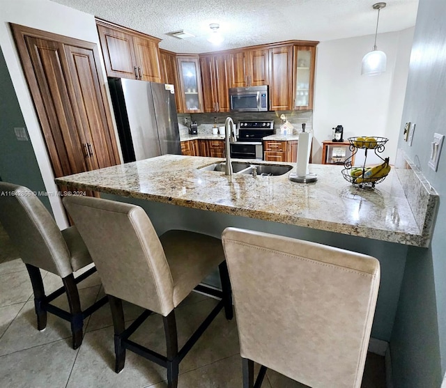 kitchen with light stone countertops, appliances with stainless steel finishes, tasteful backsplash, hanging light fixtures, and sink