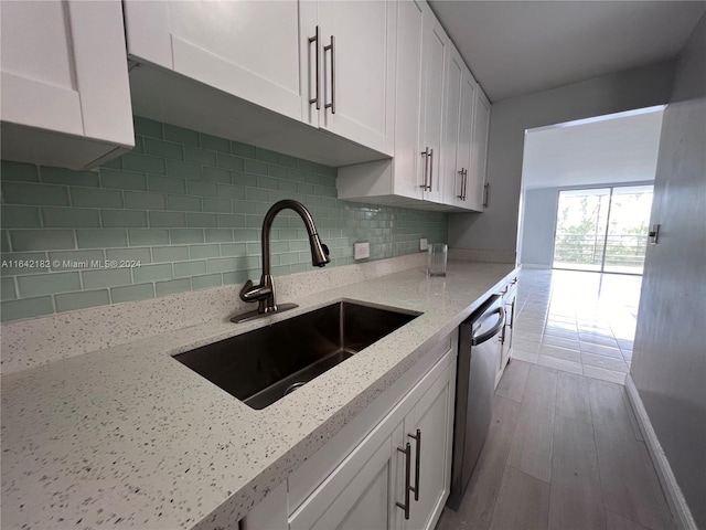 kitchen with decorative backsplash, hardwood / wood-style floors, white cabinets, light stone counters, and dishwasher