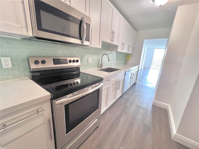 kitchen featuring backsplash, sink, light wood-type flooring, appliances with stainless steel finishes, and white cabinets