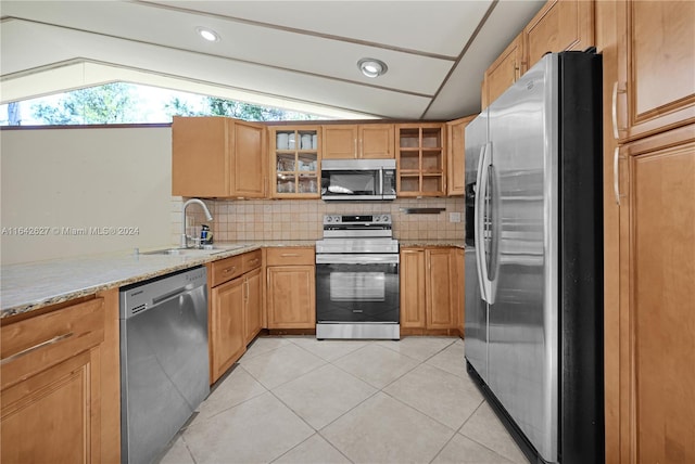 kitchen featuring decorative backsplash, appliances with stainless steel finishes, light stone countertops, sink, and lofted ceiling