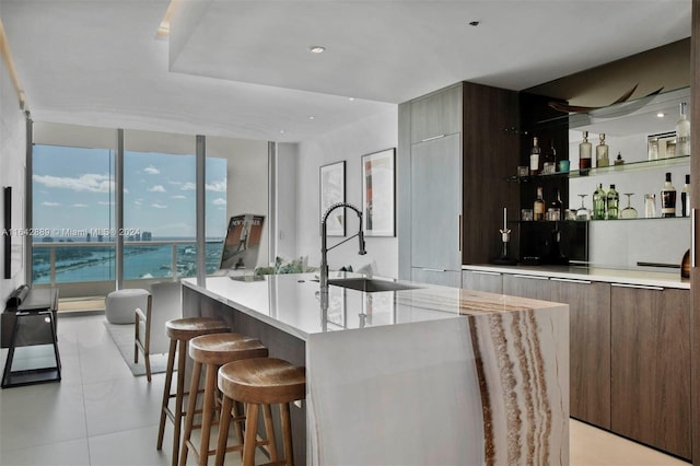 kitchen with a kitchen breakfast bar, sink, an island with sink, light tile patterned floors, and a wall of windows