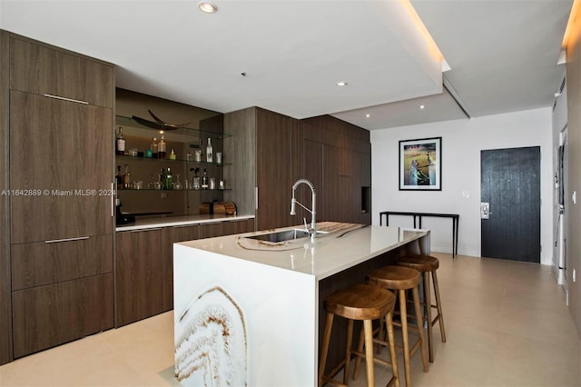 kitchen with sink, an island with sink, light tile patterned floors, and dark brown cabinetry