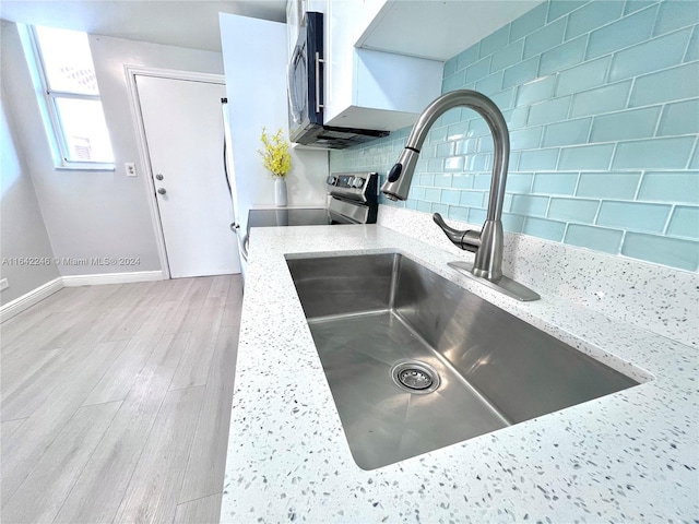 kitchen with light wood-type flooring, backsplash, sink, and light stone countertops