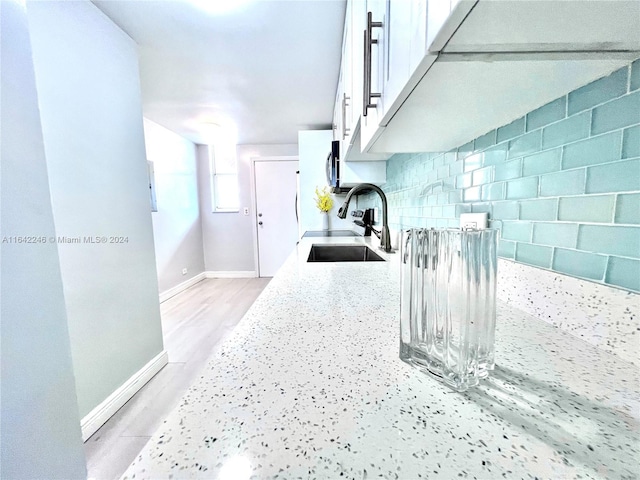 kitchen with decorative backsplash, light hardwood / wood-style flooring, white cabinets, light stone counters, and sink