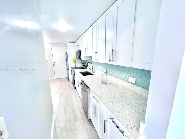 kitchen with tasteful backsplash, appliances with stainless steel finishes, light stone countertops, light wood-type flooring, and white cabinetry