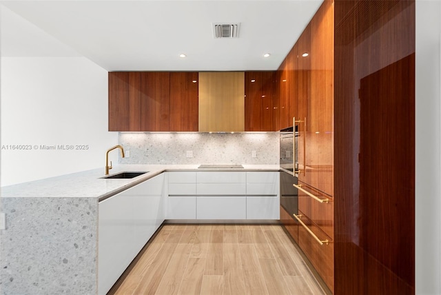 kitchen featuring black electric stovetop, light wood-type flooring, tasteful backsplash, sink, and white cabinets