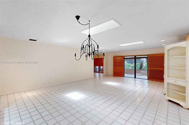 tiled spare room featuring a notable chandelier and a skylight