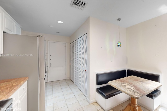 kitchen featuring light tile patterned floors, light countertops, visible vents, freestanding refrigerator, and white cabinetry