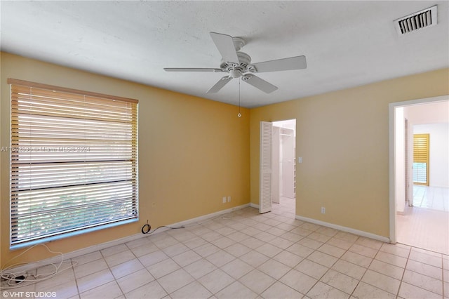 empty room with light tile patterned floors, ceiling fan, visible vents, and baseboards