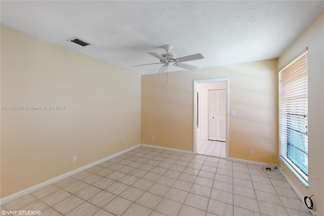 empty room featuring light tile patterned floors, a textured ceiling, a ceiling fan, visible vents, and baseboards