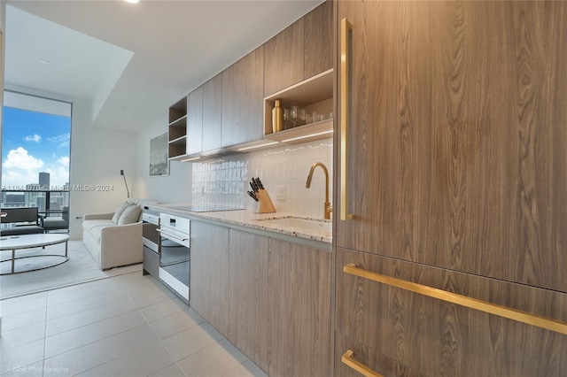 kitchen featuring black electric stovetop, light stone counters, tasteful backsplash, sink, and oven