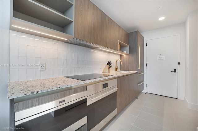 kitchen featuring light stone counters, sink, backsplash, light tile patterned floors, and stainless steel oven